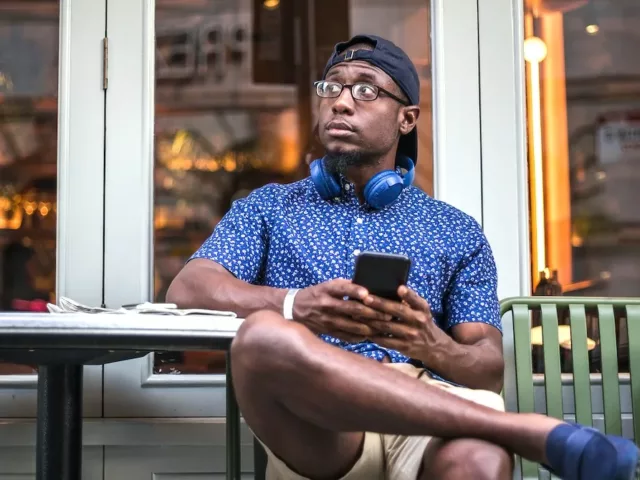 Concerned wearing a hat at cafe on phone, searching if hats cause hair loss in men