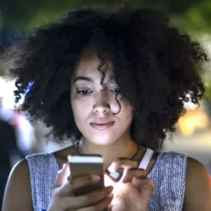 Woman on street using cell phone, realizing that blue light from technology is damaging her skin