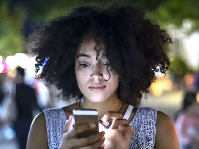 Woman on street using cell phone, realizing that blue light from technology is damaging her skin