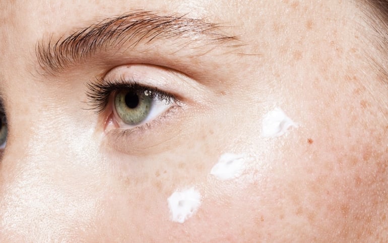 Woman with freckles applying blue light skincare