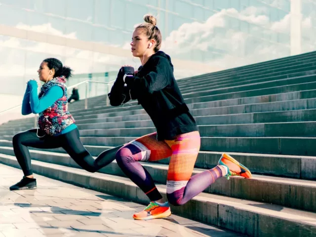 Two women doing lunges on stairs to reap the health benefits of strength training