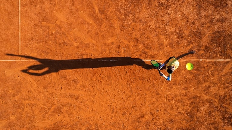 Man serving for a tennis match on clay court, reducing stress through exercising with a friend