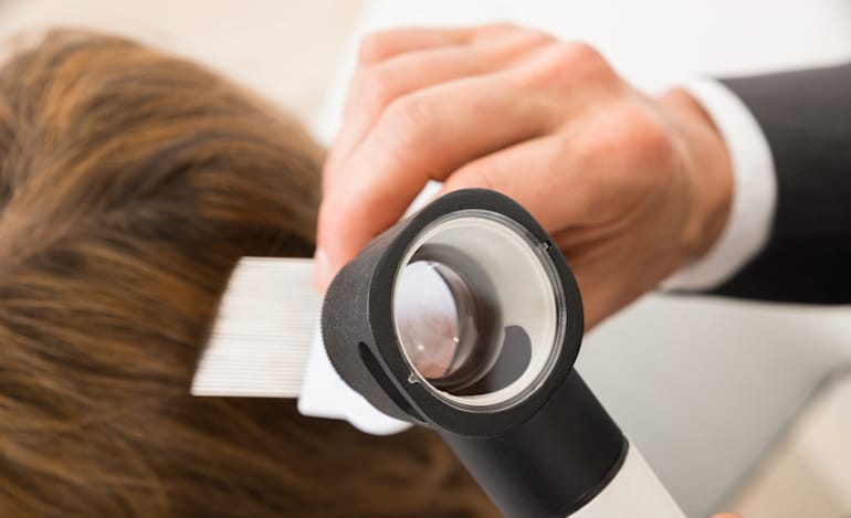 Trichologist aka hair doctor looking at a man's scalp and hair health through a microscope to figure out how to combat hair loss