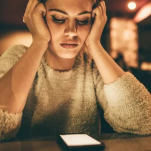 Woman at bar alone looking at phone, waiting for someone to text her, needing to learn how to deal with ghosting