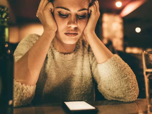 Woman at bar alone looking at phone, waiting for someone to text her, needing to learn how to deal with ghosting