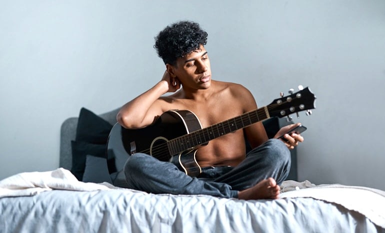 Man with guitar in bed looking at his phone, trying to learn how to get over being ghosted