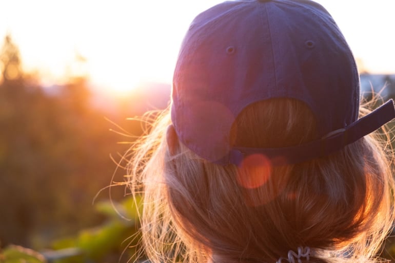 Behind shot of woman wearing a baseball hat in the sun to protect her hair and scalp from UV damage