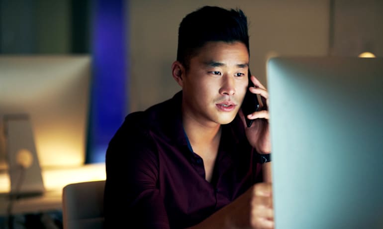 Man on computer and phone, illustrating that blue light can cause skin damage