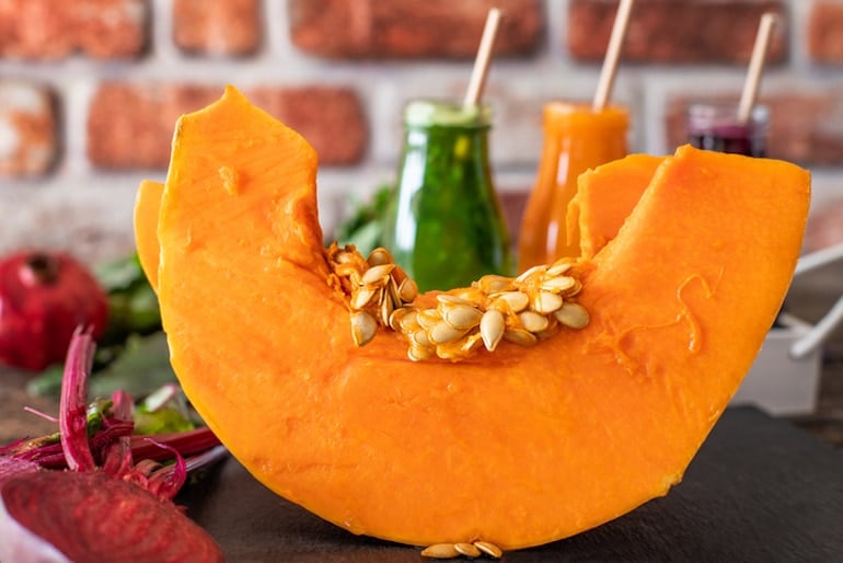 Cut pumpkin with seeds in front of healthy pressed juices, to illustrate the health benefits of pumpkin