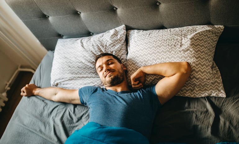 Man waking up and stretching in bed after a good night's sleep