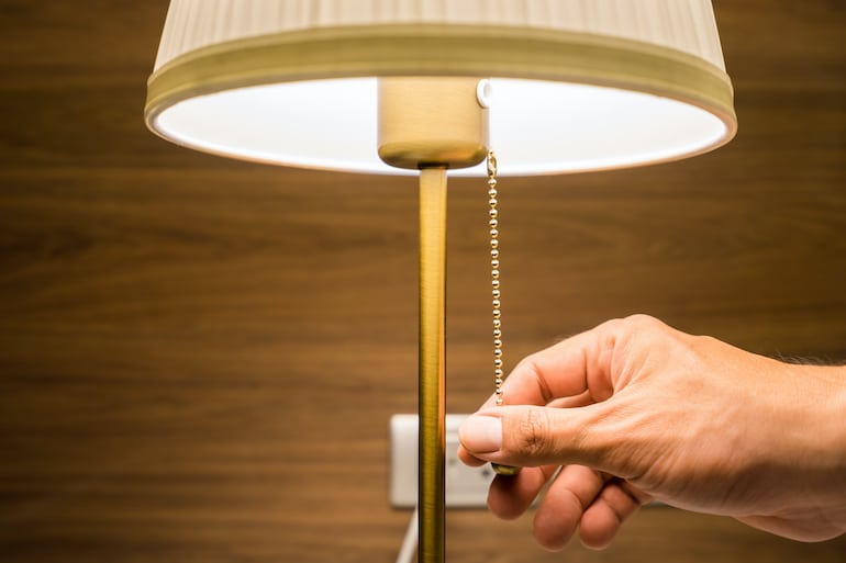 Person's hand turning off bedside lamp to prepare for sleep