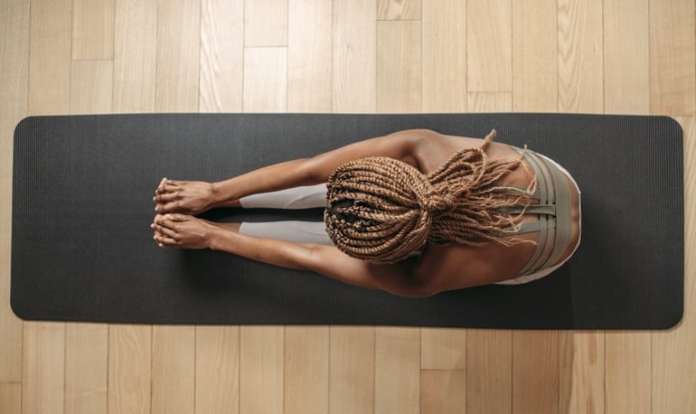 Overhead shot of woman stretching on yoga mat; yoga and Pilates low-impact training concept