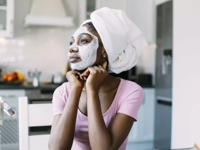 Woman sitting at kitchen table with a DIY hydrating face mask on to save her dry skin in the winter