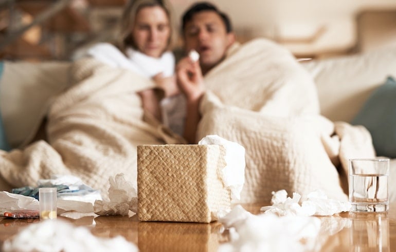 Sick couple on couch with dirty tissues