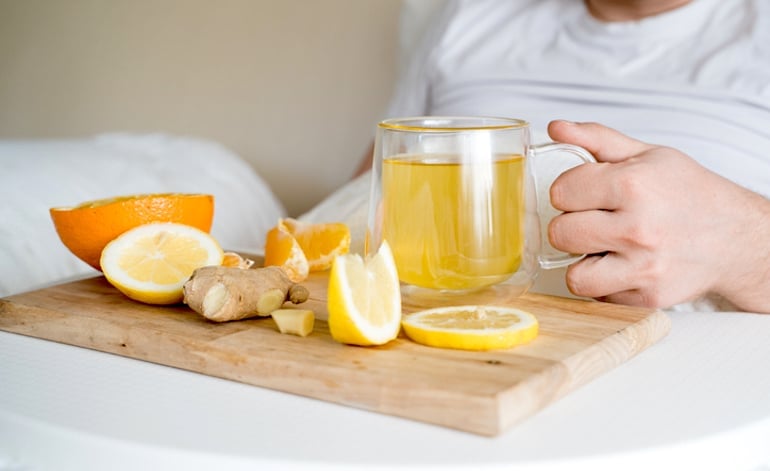 Man drinking ginger tea with honey in bed, which has three of the best foods to eat when sick