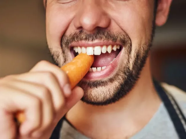 Man chewing into a carrot to illustrate how many times you're supposed to chew your food