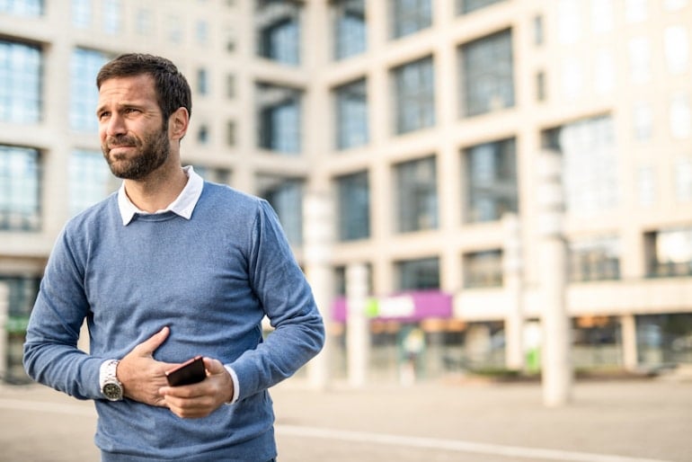 Man touching stomach in pain while walking, wondering if farting is healthy and normal