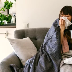 Woman sick at home on couch and drinking ginger tea, some of the best foods to eat when you're sick