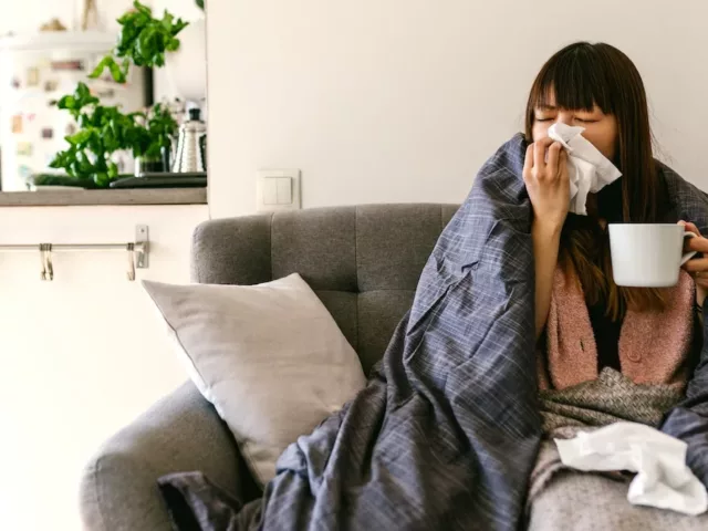 Woman sick at home on couch and drinking ginger tea, some of the best foods to eat when you're sick