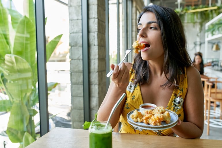 Woman eating cauliflower in a restaurant, a food rich in fiber and sulfur that can cause farting