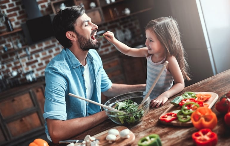 Daughter feeding her dad veggies to illustrate why we should chew our food properly