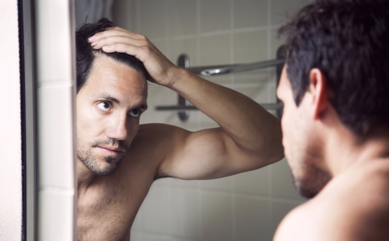 Man checking hair line in the mirror to investigate hair loss