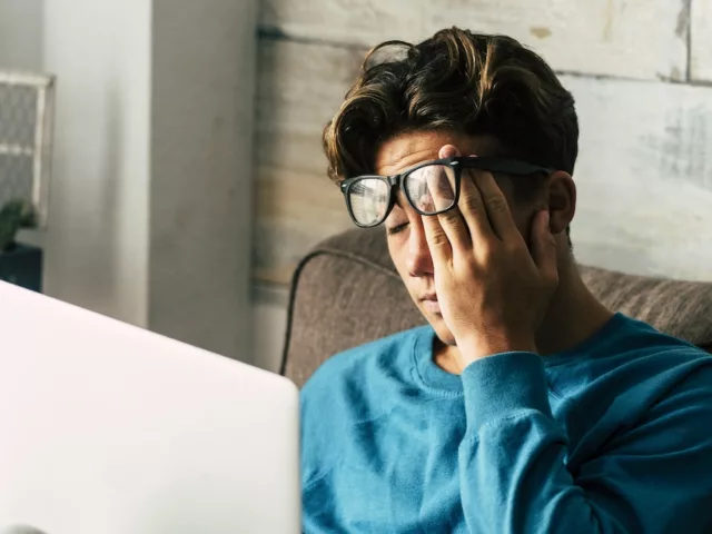 Fatigued man experiencing fatigue from hormonal imbalance at home on his laptop