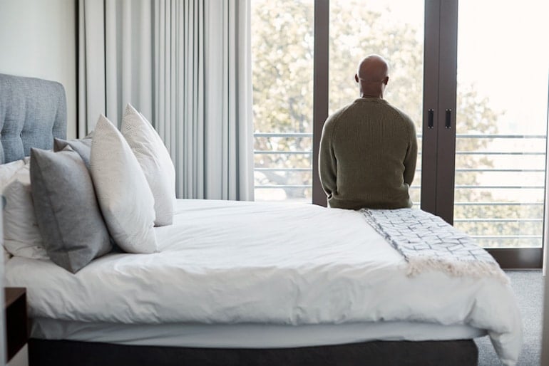 Man sitting on bed looking outside, tired from symptoms of male hormonal imbalance