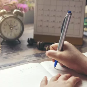 Woman at desk writing in her self-care planner to map out her daily activities, goals, and reflections