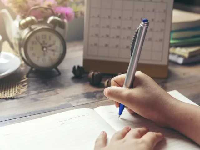 Woman at desk writing in her self-care planner to map out her daily activities, goals, and reflections