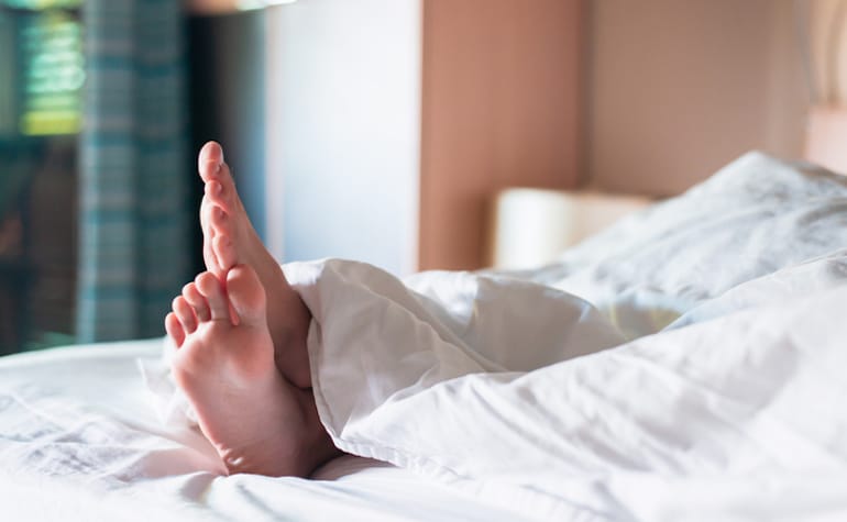 Person's foot under weighted blanket in bed to reap benefits for stress and sleep