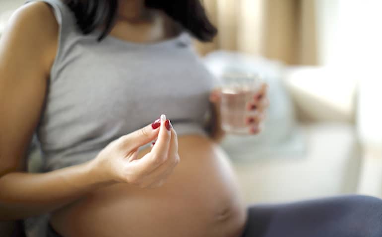 Pregnant woman taking supplements to illustrate essential vitamins for pregnant women