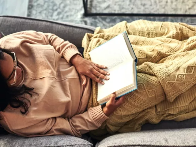 Woman reading a book on the couch as a stress reduction technique