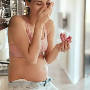 Pregnant woman with cravings eating doughnuts on kitchen counter