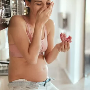 Pregnant woman with cravings eating doughnuts on kitchen counter