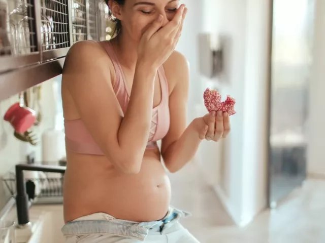 Pregnant woman with cravings eating doughnuts on kitchen counter