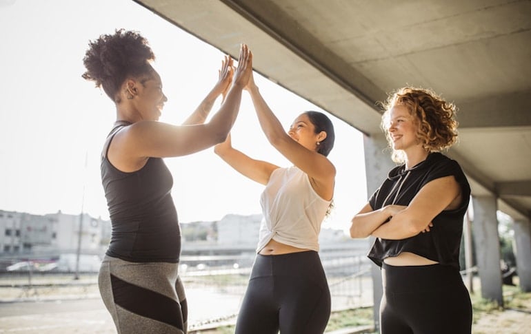 Women high-fiving after working out, with tracking progress and celebrating small wins as one of Jen Sincero's badass habits