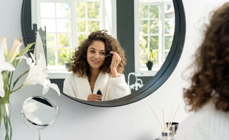 Woman applying hyaluronic acid serum, one of the best ingredients for dry skin, while looking in the mirror