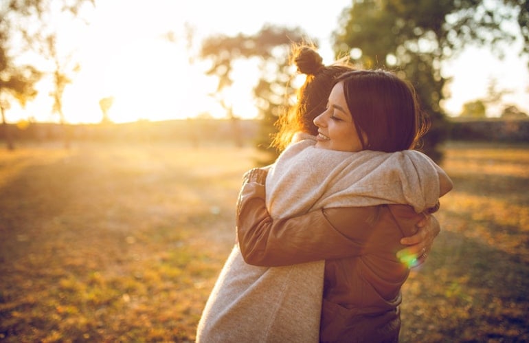 Friends hugging outdoors, showing support helps reduce stress