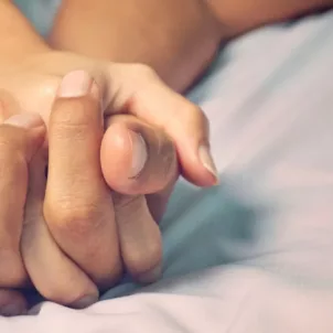 Close up of couple's hands intertwined in bed, to illustrate the idea of how often couples should have sex