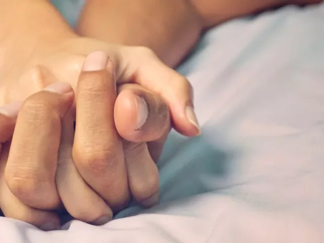 Close up of couple's hands intertwined in bed, to illustrate the idea of how often couples should have sex