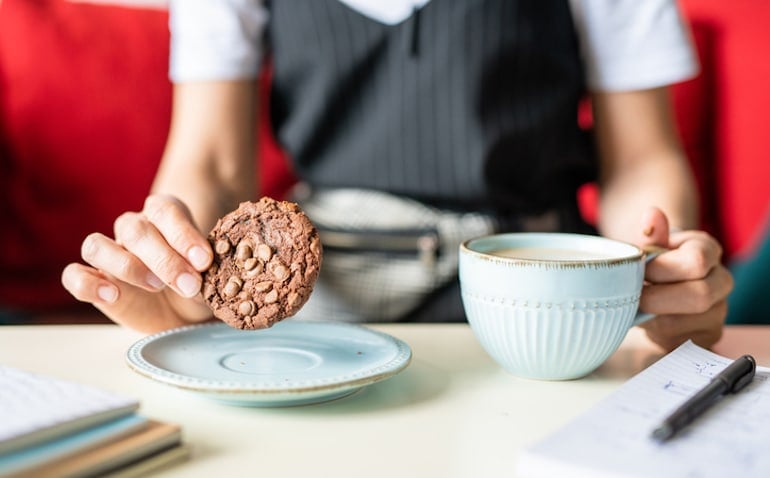 Woman having a cookie with coffee, which is a habit that needs changing if you want to eat healthier