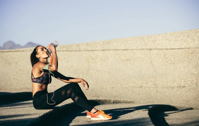 Woman drinking water after running and sweating outdoors to illustrate why it's important to stay hydrated