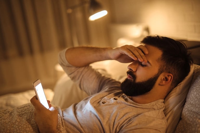 Man worrying in bed on his phone, recognizing triggers in order to create good habits