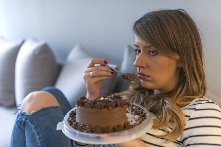 Sad stressed woman eating a cake alone