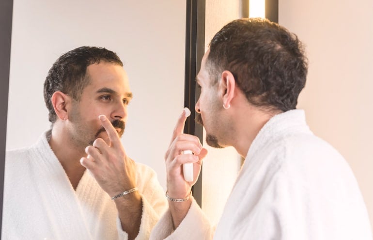 Man applying acne-fighting treatment in the mirror to get rid of blind pimples