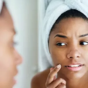 Woman freshly out of shower looking at her skin in mirror, trying to discover if she has blind pimples and how to treat them