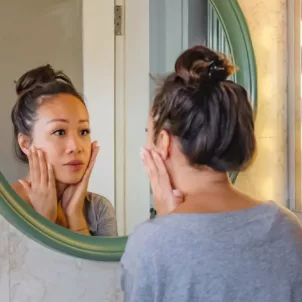 Worried woman looking at her face in the mirror and investigating skin purging from a new product