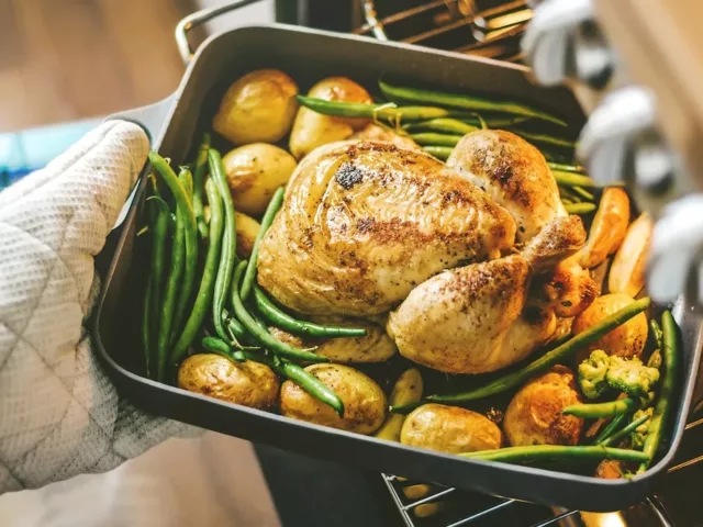 Dietitian taking a one-pan meal of chicken, green beans, and potatoes out of the oven as part of her mindful eating dinner plan