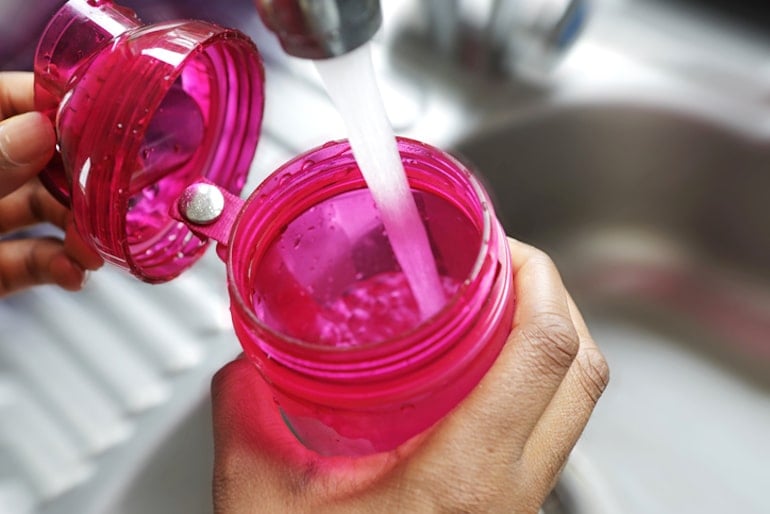 Woman's hand filling water bottle at the sink to start her day by hydrating and taking vitamins